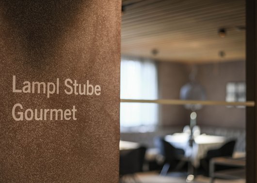 Lampl Stube: il nostro ristorante a Castelrotto Targa Lampl Stube Gourmet su muro con interno sfocato sullo sfondo