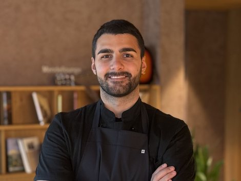4-Sterne-Hotel Lamm am Fuße der Seiser Alm Lächelnder junger Mann mit Tattoo und schwarzer Schürze in einem Café