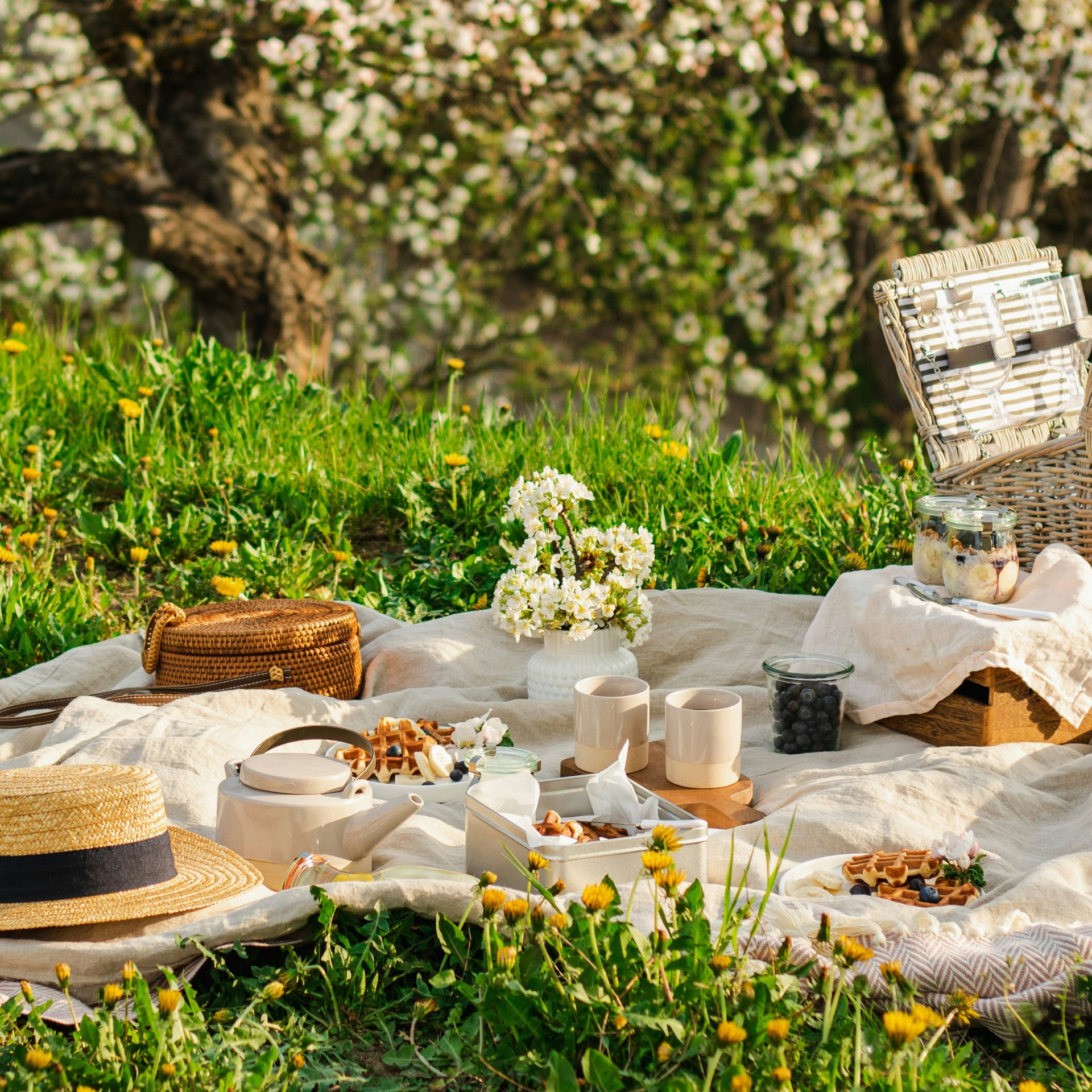 4-Sterne-Hotel Lamm am Fuße der Seiser Alm Picknick mit Korb, Hut und Snacks auf einer Wiese mit blühenden Bäumen