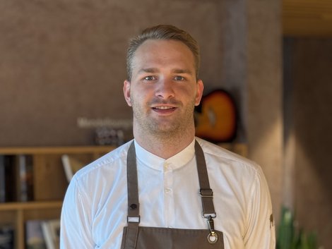4-Sterne-Hotel Lamm am Fuße der Seiser Alm Portrait eines lächelnden Mannes mit Arbeitskleidung in einem modernen Café