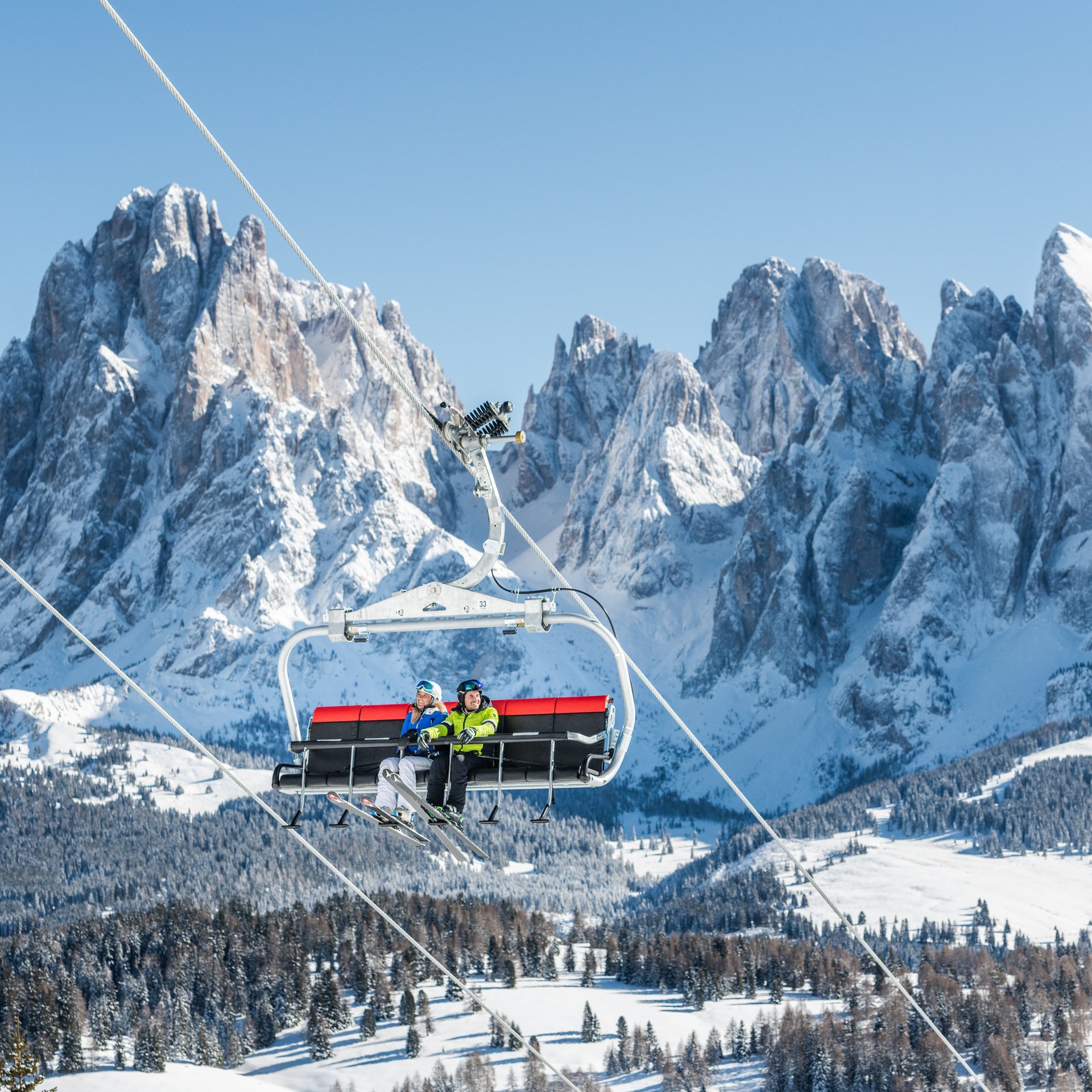 4-Sterne-Hotel Lamm am Fuße der Seiser Alm Zwei Skifahrer auf einem Skilift vor verschneiten Bergen