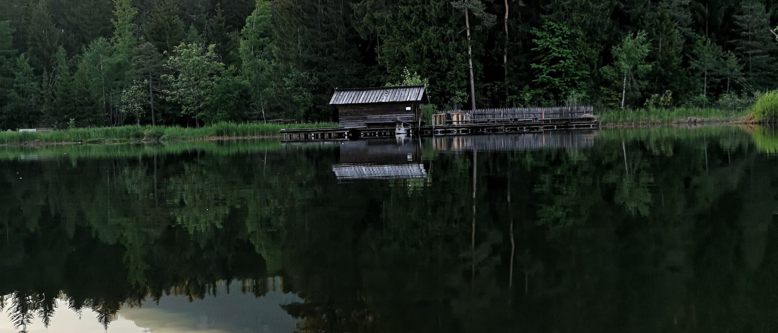Der 7-Weiher-Weg am Fuße des Schlerns – wandern Sie los! Bergsee mit Wald und Hütte, Bergspitze im Hintergrund, Spiegelung im Wasser