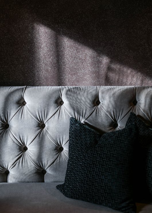 Gourmet restaurant in South Tyrol: Lampl Stube Sunlight on gray velvet sofa with black pillows against dark wall