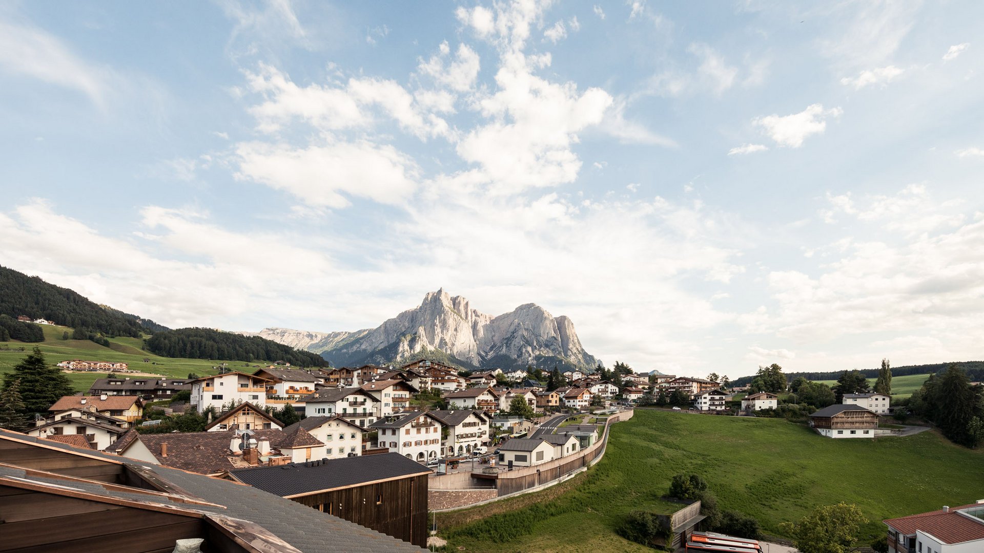 4-Sterne-Hotel Lamm am Fuße der Seiser Alm Blick auf Dorf mit Bergen im Hintergrund unter bewölktem Himmel