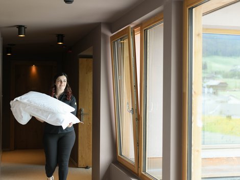 4-Sterne-Hotel Lamm am Fuße der Seiser Alm Frau trägt Kissen im Hotelflur mit Fenstern und Bergblick