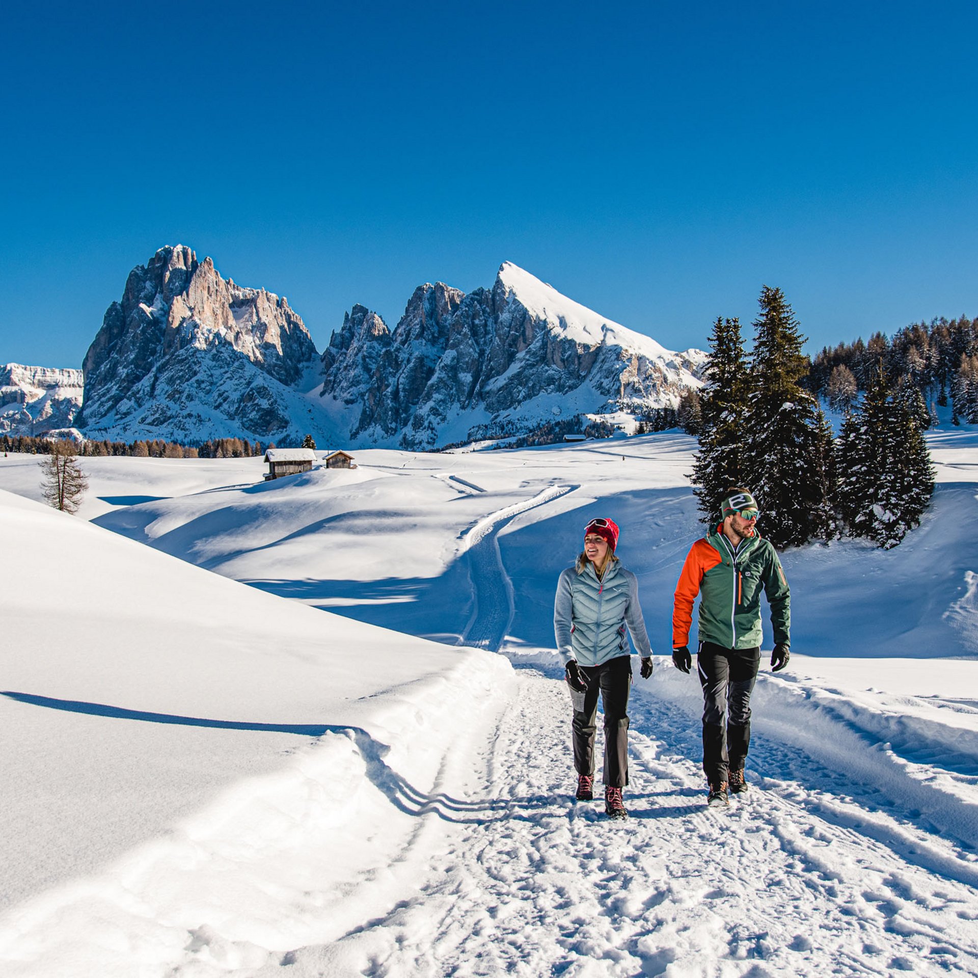 4-Sterne-Hotel Lamm am Fuße der Seiser Alm Zwei Wanderer auf verschneitem Weg mit Bergkulisse bei strahlend blauem Himmel