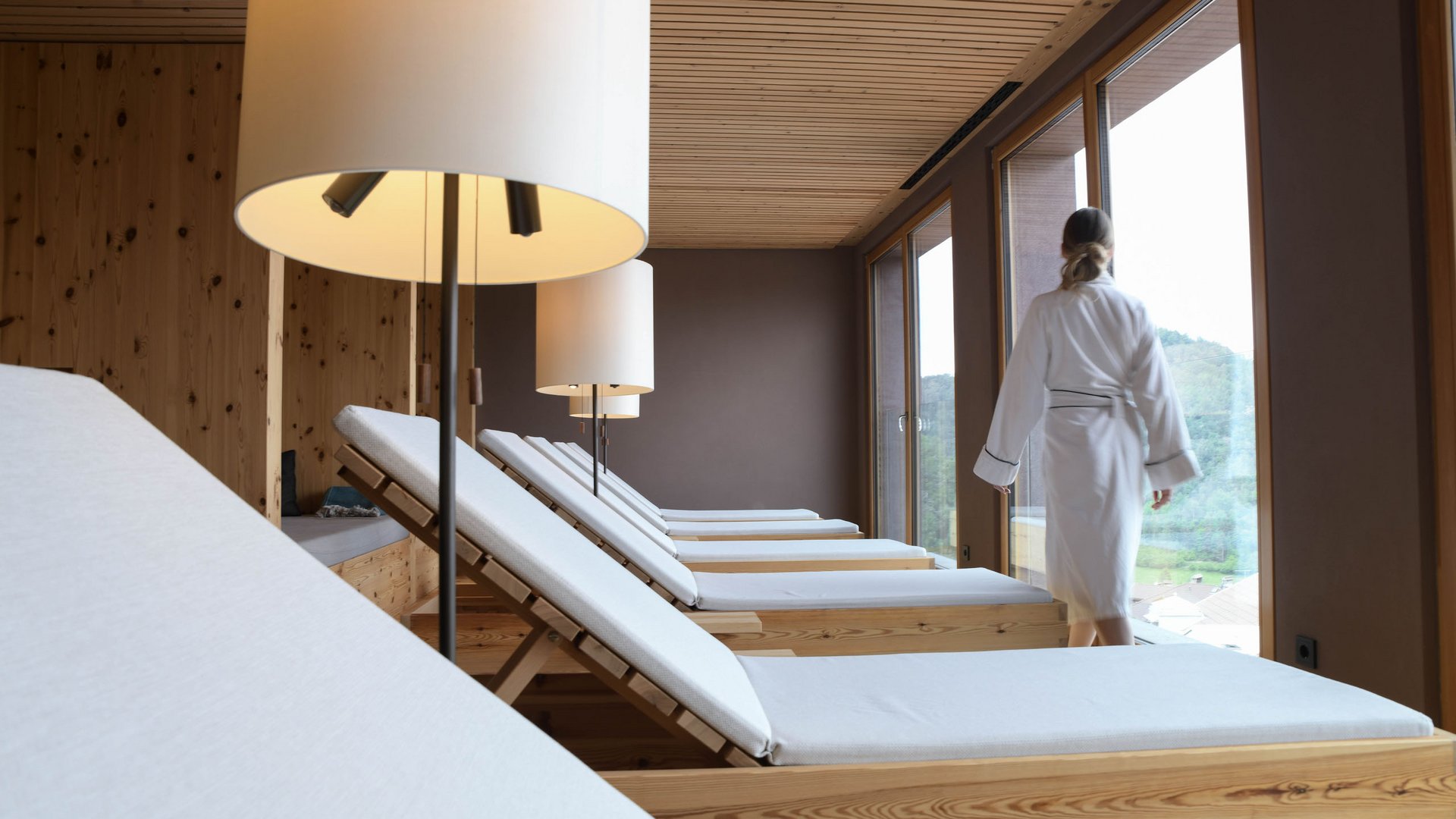 4-Sterne-Hotel Lamm am Fuße der Seiser Alm Entspannungsraum mit Liegen und einer Person im Bademantel am Fenster